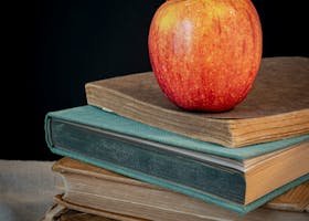 A classic red apple placed on a stack of aged books with a black background.