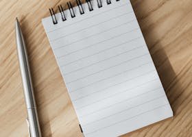 From above of small opened notepad and stylish silver pen placed on wooden table near laptop